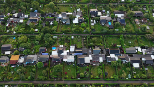 Aerial drone view of Strandhoj community garden in in Copenhagen, Denmark, with small houses, lush greenery, and vibrant private plots separated by hedges - Starpik Stock
