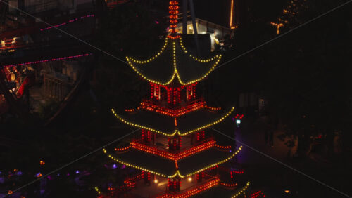 Aerial drone view of a lit pagoda and surrounding landscape in Tivoli Gardens, Copenhagen, Denmark, at night - Starpik Stock