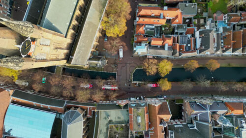 Aerial drone view of a narrow canal flanked by rows of historic Dutch townhouses with red-tiled roofs and tree-lined walkways in Delft, Netherlands - Starpik Stock