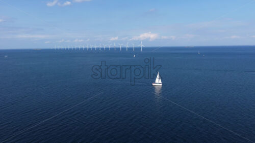 Aerial drone view of a sailboat cruising in Oresund waters, with a line of offshore wind turbines in the background - Starpik Stock