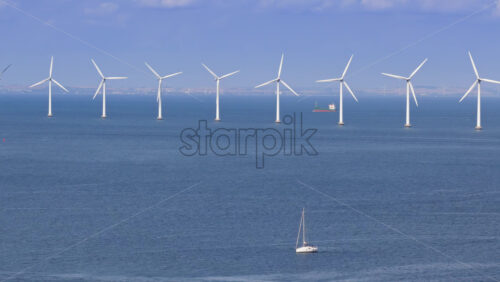 Aerial drone view of a sailboat cruising in Oresund waters, with a line of offshore wind turbines in the background - Starpik Stock