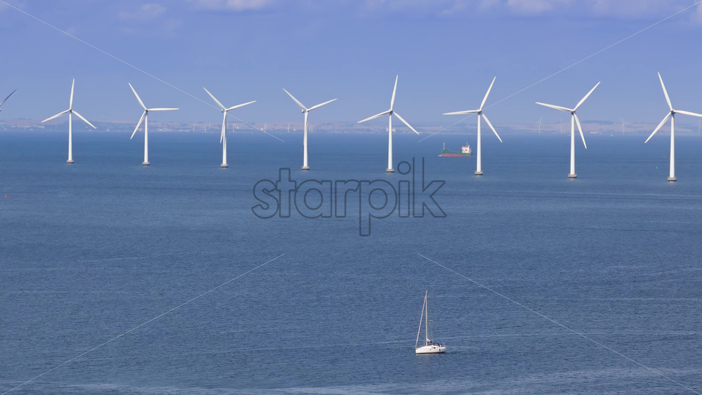 Aerial drone view of a sailboat cruising in Oresund waters, with a line of offshore wind turbines in the background - Starpik Stock