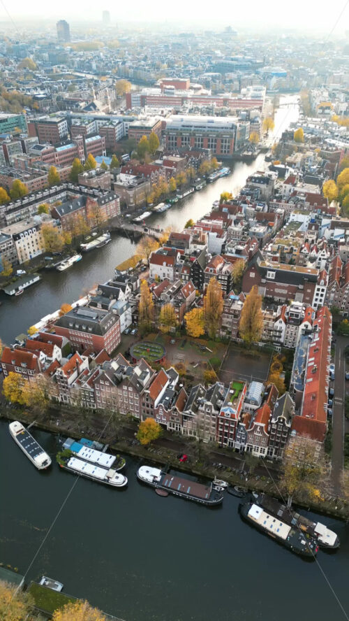 Aerial drone view of buildings surrounding a tree-lined canal in Amsterdam, Netherlands in daylight. Vertical - Starpik Stock