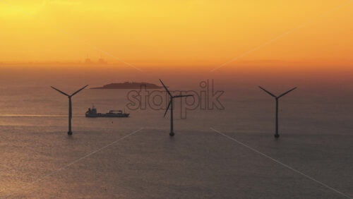 Aerial drone view of cargo ship sailing past offshore wind turbines in the Oresund Strait during a golden sunrise in Copenhagen, Denmark - Starpik Stock