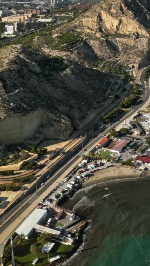 Aerial drone view of cars moving along the coastline in Alicante, Spain in daylight. Vertical - Starpik Stock
