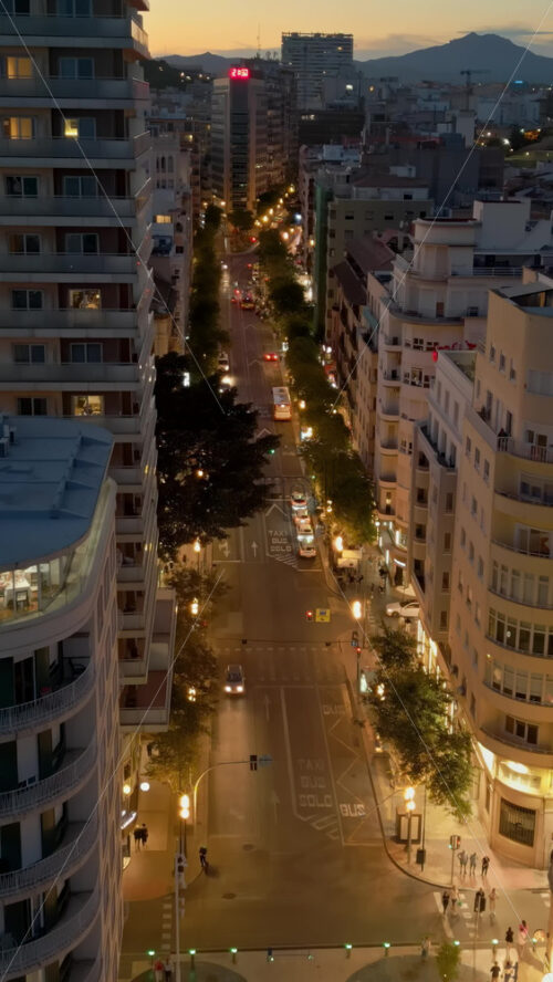 Aerial drone view of cars moving between the buildings in Alicante, Spain at sunset. Vertical - Starpik Stock