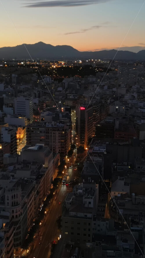 Aerial drone view of cars moving between the buildings in Alicante, Spain in the evening. Vertical - Starpik Stock