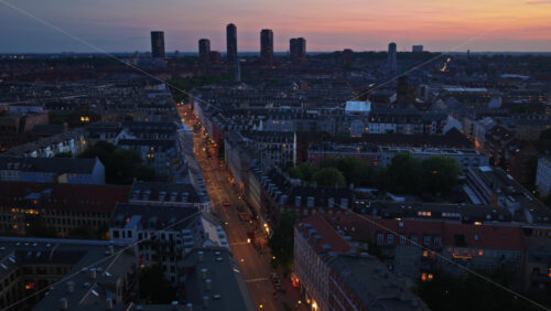 Aerial drone view of long illuminated streets lined with historic Danish townhouses and apartments, glowing warmly as night falls in Copenhagen - Starpik Stock