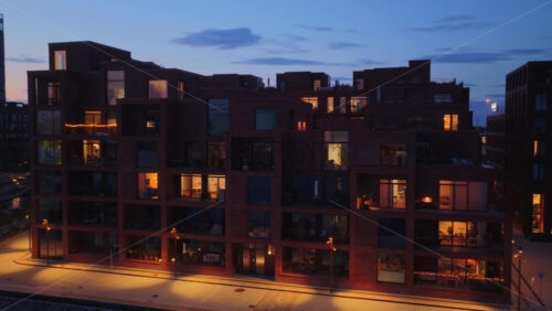 Aerial drone view of modern apartments along the waterfront promenade in Copenhagen, Denmark, with warm lights reflecting on the water - Starpik Stock