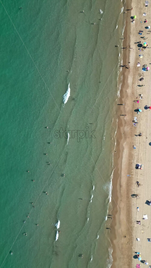 Aerial drone view of people relaxing on the beach with hitting the shore in Alicante, Spain. Vertical - Starpik Stock