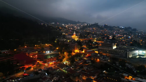 Aerial drone view of skyscrapers lighting up the skyline against the Andean foothills in Bogota, Colombia in the evening - Starpik Stock