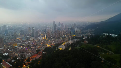 Aerial drone view of skyscrapers lighting up the skyline against the Andean foothills in Bogota, Colombia in the evening - Starpik Stock