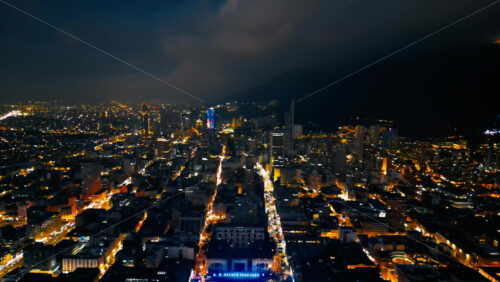 Aerial drone view of skyscrapers lighting up the skyline against the Andean foothills in Bogota, Colombia in the evening - Starpik Stock