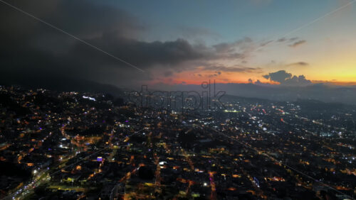 Aerial drone view of skyscrapers lighting up the skyline against the Andean foothills in Bogota, Colombia in the evening - Starpik Stock
