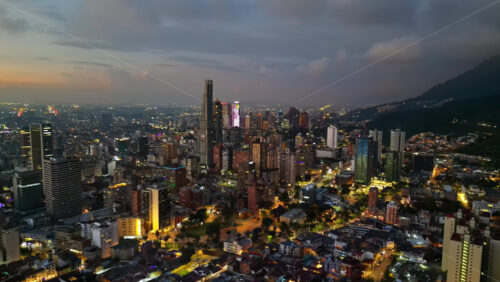 Aerial drone view of skyscrapers lighting up the skyline against the Andean foothills in Bogota, Colombia in the evening - Starpik Stock