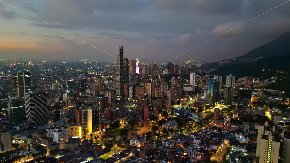 Aerial drone view of skyscrapers lighting up the skyline against the Andean foothills in Bogota, Colombia in the evening - Starpik Stock
