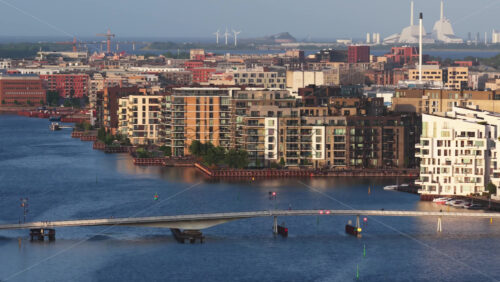 Aerial drone view of the Bryggebroen Quay Bridge with modern waterfront apartments in Copenhagen, Denmark with canals and wind turbines in the distance - Starpik Stock