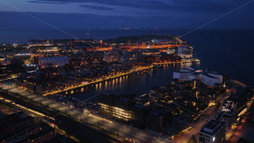 Aerial drone view of the Copenhagen harbor, modern waterfront buildings, and glowing streets illuminated at night in Denmark - Starpik Stock