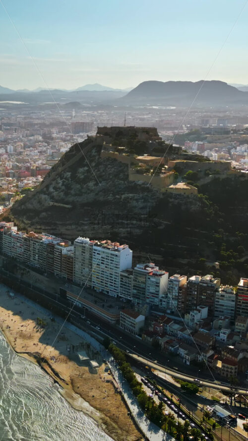 Aerial drone view of the Santa Barbara Castle on the coast of Alicante, Spain with the city and the sea in daylight. Vertical - Starpik Stock
