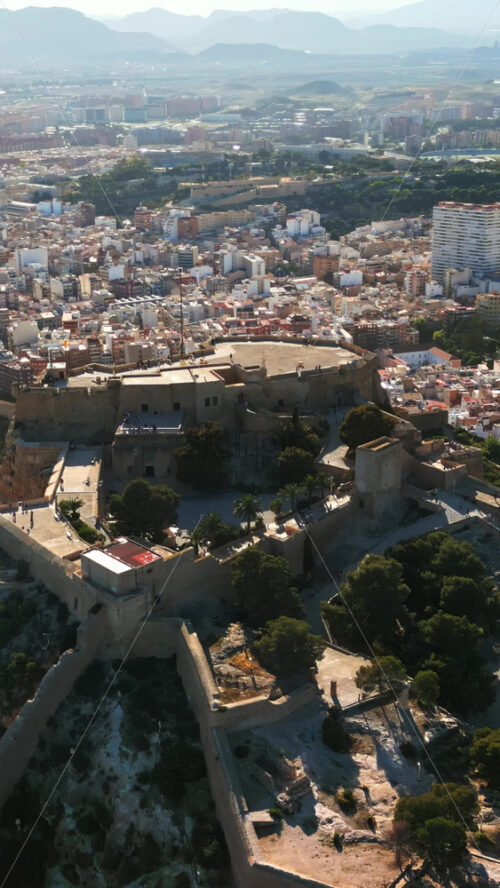 Aerial drone view of the Santa Barbara Castle on the coast of Alicante, Spain with the city on the background. Vertical - Starpik Stock