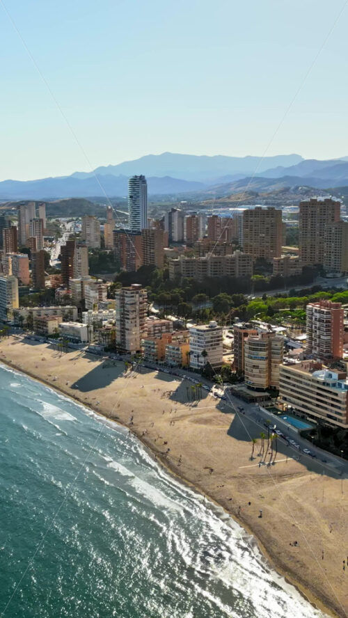 Aerial drone view of the buildings along the coastline and the sea in Benidorm, Spain in daylight. Vertical - Starpik Stock