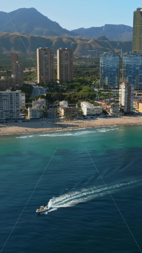 Aerial drone view of the buildings along the coastline with people parasailing in the sea in Benidorm, Spain in daylight. Vertical - Starpik Stock