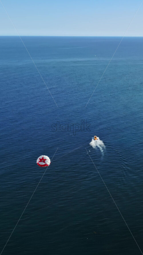Aerial drone view of the buildings along the coastline with people parasailing in the sea in Benidorm, Spain in daylight. Vertical - Starpik Stock