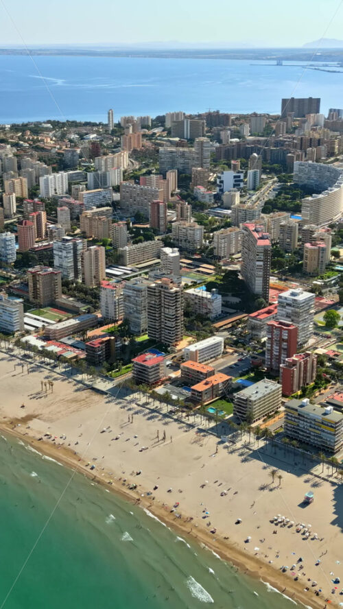 Aerial drone view of the buildings along the coastline with people relaxing on the beach in Alicante, Spain in daylight. Vertical - Starpik Stock
