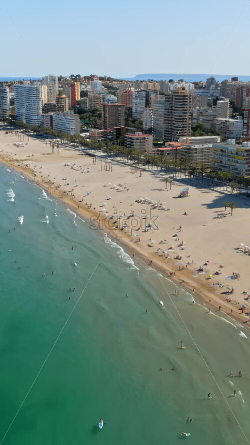 Aerial drone view of the buildings along the coastline with people relaxing on the beach in Benidorm, Spain in daylight. Vertical - Starpik Stock