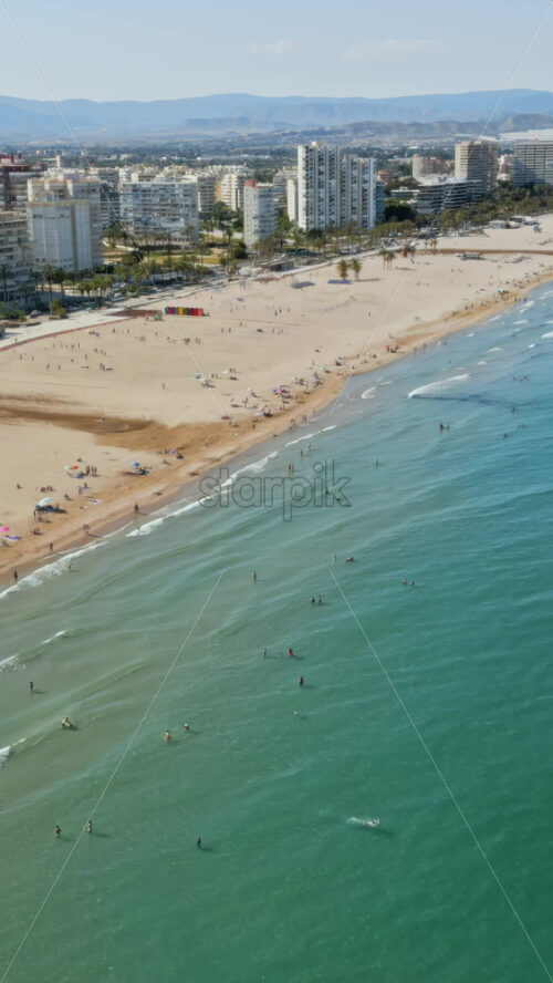 Aerial drone view of the buildings along the coastline with people relaxing on the beach in Benidorm, Spain in daylight. Vertical - Starpik Stock