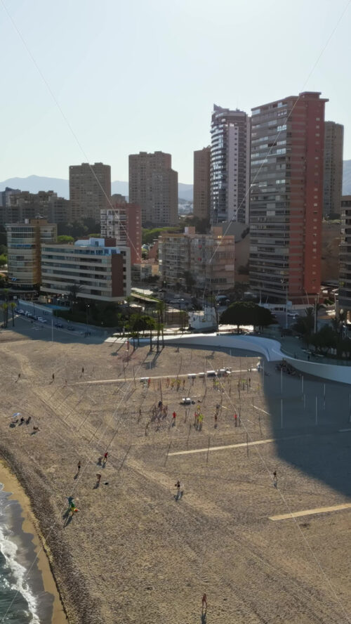 Aerial drone view of the buildings along the coastline with people relaxing on the beach in Benidorm, Spain in daylight. Vertical - Starpik Stock