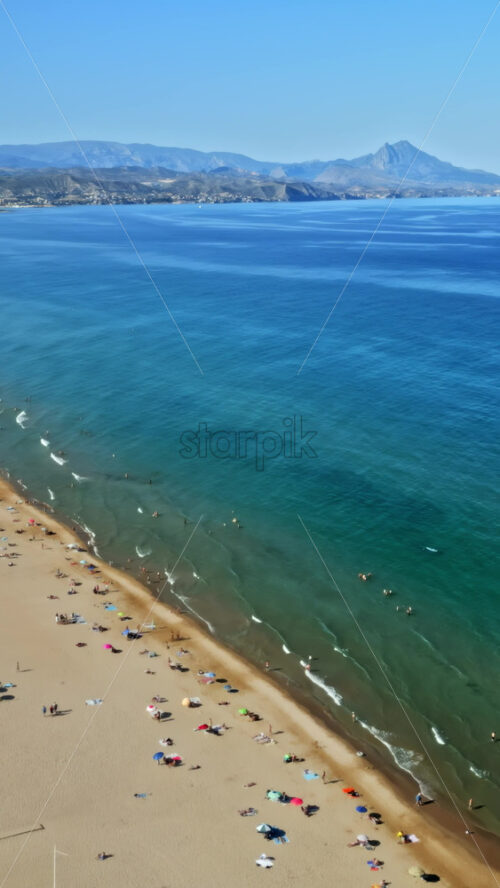 Aerial drone view of the buildings along the coastline with people relaxing on the beach in daylight. Vertical - Starpik Stock