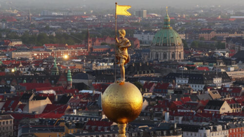 Aerial drone view of the golden statue atop a sphere on the Church of Our Saviour overlooking the Copenhagen skyline, with Frederik’s Church dome in the background in Denmark - Starpik Stock