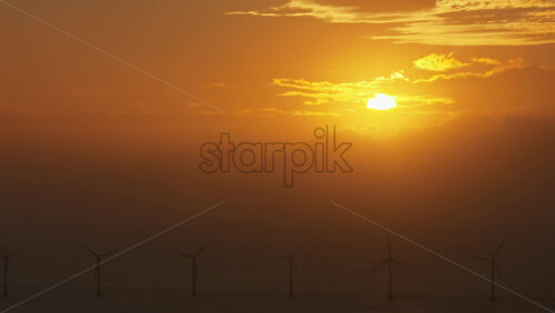 Aerial drone view of the golden sun over the Danish coast, casting light on offshore wind turbines - Starpik Stock