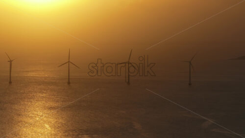 Aerial drone view of the golden sun over the Danish coast, casting light on offshore wind turbines. Copenhagen, Denmark - Starpik Stock