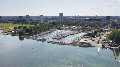 Aerial drone view of the marina filled with sailboats, surrounded by residential blocks and the green coast in Copenhagen, Denmark - Starpik Stock