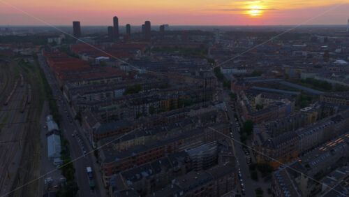 Aerial drone view of warm evening light over the rooftops of Vesterbro and Frederiksberg, with industrial chimneys and towers on the horizon in Copenhagen, Denmark - Starpik Stock