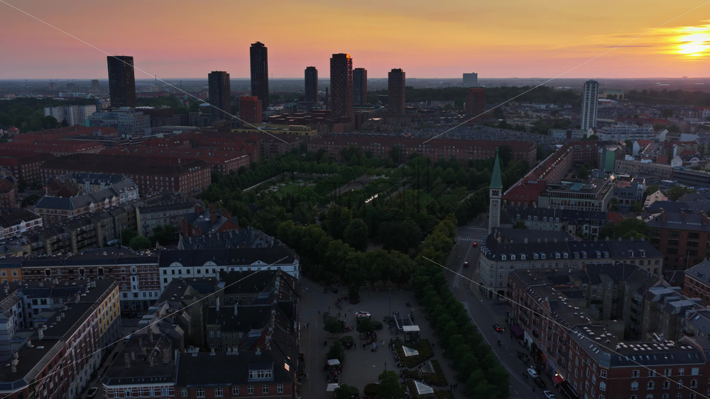 Aerial drone view of warm evening light over the rooftops of Vesterbro and Frederiksberg, with industrial chimneys and towers on the horizon in Copenhagen, Denmark - Starpik Stock