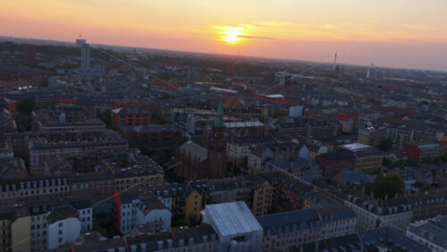 Aerial drone view of warm evening light over the rooftops of Vesterbro and Frederiksberg, with industrial chimneys and towers on the horizon in Copenhagen, Denmark - Starpik Stock
