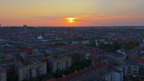Aerial drone view of warm evening light over the rooftops of Vesterbro and Frederiksberg, with industrial chimneys and towers on the horizon in Copenhagen, Denmark - Starpik Stock