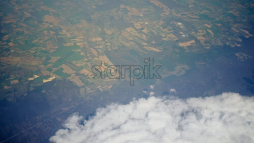 Aerial view of white, fluffy clouds above fields seen from an airplane window - Starpik Stock