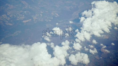 Aerial view of white, fluffy clouds above fields seen from an airplane window - Starpik Stock