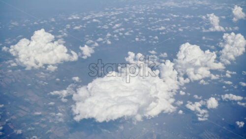 Aerial view of white, fluffy clouds above fields seen from an airplane window - Starpik Stock