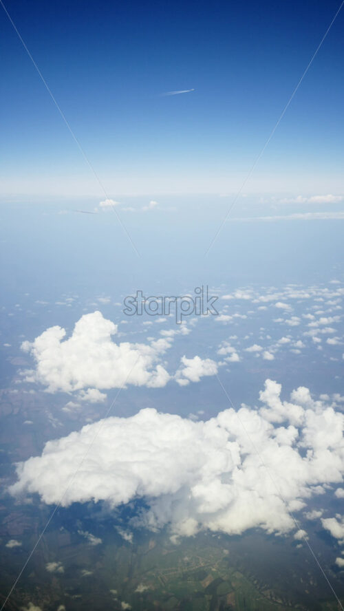 Aerial view of white, fluffy clouds above fields seen from an airplane window. Vertical - Starpik Stock