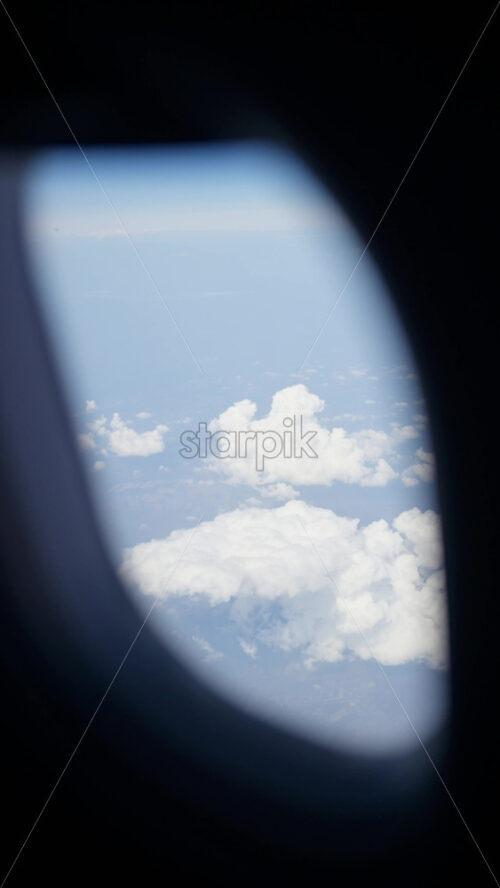 Aerial view of white, fluffy clouds above fields seen from an airplane window. Vertical - Starpik Stock