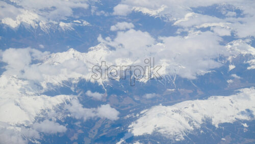 Aerial view of white, fluffy clouds above snowy mountains seen from an airplane window - Starpik Stock
