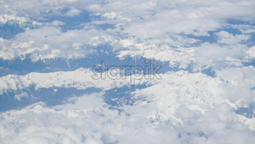 Aerial view of white, fluffy clouds above snowy mountains seen from an airplane window - Starpik Stock