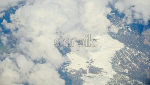 Aerial view of white, fluffy clouds above snowy mountains seen from an airplane window - Starpik Stock