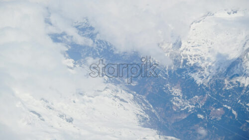 Aerial view of white, fluffy clouds above snowy mountains seen from an airplane window - Starpik Stock