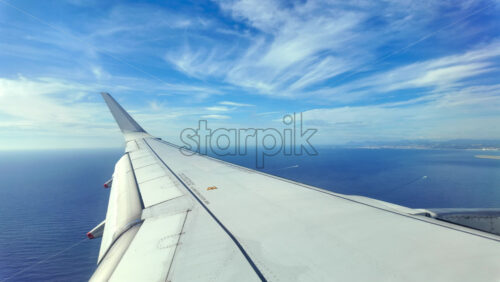 Aircraft wing glides above layered clouds and shimmering sea - Starpik Stock